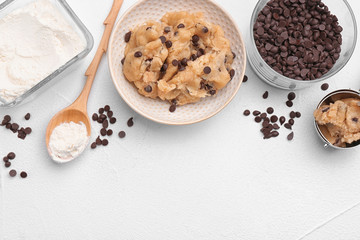 Flat lay composition with cookie dough, chocolate chips and flour on light background