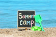 Little blackboard with text SUMMER CAMP and toys on sand near sea