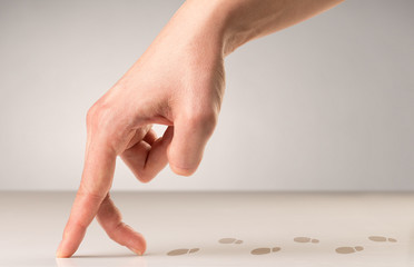 Female fingers walking on white surface with footsteps behind it