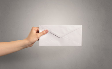 Female hand holding coloured and white envelope with empty wall background
