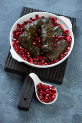 Wall Mural - White plate with dolmades or dolma and pomegranate seeds on a black wooden serving board, blue stone background, studio shot