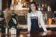 © weedezign - Asian female barista wear jean apron place her hand on counter bar and smiling to customer,cafe service concept,owner business start up