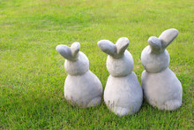 Three Rabbit Dolls Made From Cement Are On The Green Grass Field Used As Gardened Decoration.