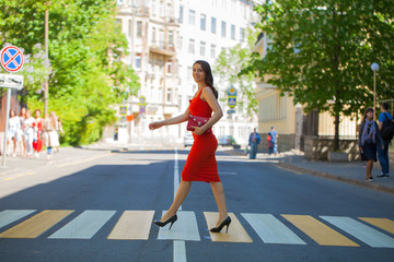 Wall Mural - Lady in red. Young woman in dress crosses the street on a pedestrian crossing