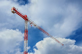 Fototapeta  - Red and white construction crane among beautiful clouds