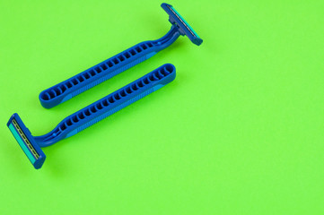 Two new blue plastic disposable razors with two blades and humid strip on blank green paper