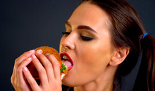 Woman eating hamburger. Girl wants to eat burger. Portrait of person with good appetite have greedily dinner delicious sandwich on black background. How to look sexy when you eat.