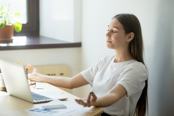 Concentrated female worker meditating in office, controlling emotions, looking for balance, relieving work stress during break. Woman sitting in chair relaxing, no pressure, mental health