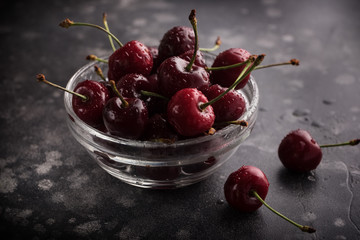 Sweet ripe cherries in glass bowl on a table. Beautiful juicy berries on the dark background.