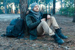 © Andrii - adult handsome Male traveler Sits On autumn pine forest Near tree, Holding At Tablet Recreation Resting Travel Destination Concept