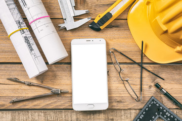 Architect workplace. Smartphone with white, blank screen, project construction blueprints and engineering tools on wooden desk, copy space, top view