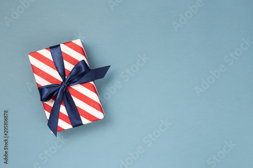 Gift box wrapped in red striped paper and tied with blue bow on blue-gray bac...