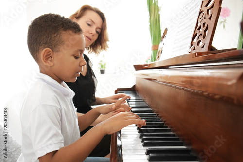 Fotomural African-American boy with teacher learning to play piano indoors