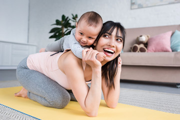 little child piggybacking on happy mother while she standing on yoga mat at home