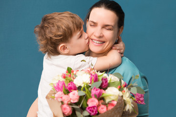 Wall Mural - Cute little child  hugging and kissing her mother and offering flowers on a blue background. Mother's day, birthday