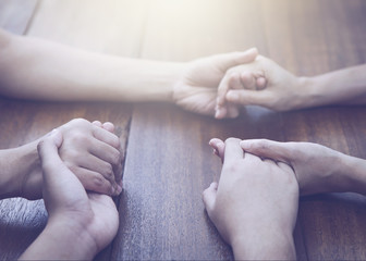 Wall Mural - three people holding hands and pray together on wooden table