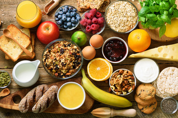 Wall Mural - Healthy breakfast ingredients, food frame. Granola, egg, nuts, fruits, berries, toast, milk, yogurt, orange juice, cheese, banana, apple on wooden rustic background, top view, copy space.