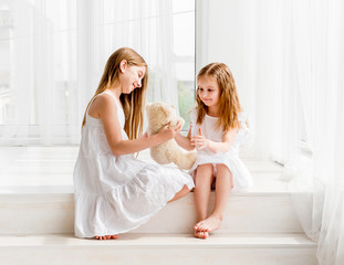 little girl giving her teddy bear toy to older sister