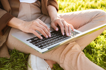 Wall Mural - Cropped photo of woman sitting on grass using laptop computer.