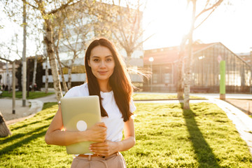 Poster - Happy woman walking in park outdoors holding laptop