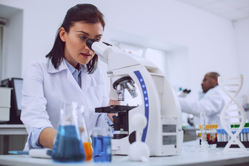 Important research. Serious experienced scientist working with her microscope and wearing a uniform