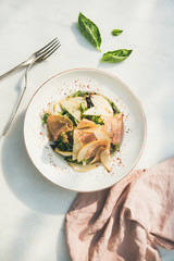 Flat-lay of fresh summer salad with smoked turkey ham and slices of pear in white plate over white table background, top view