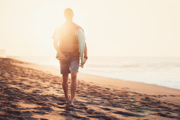 Wall Mural - Male surfer walking on the beach near the ocean with short surfboard