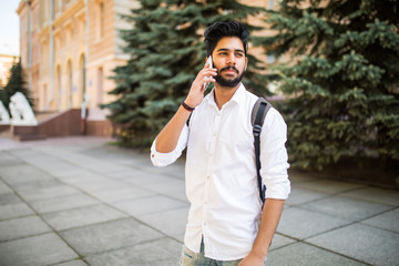 Wall Mural - Handsome young Indian student talking smartphone in the city street