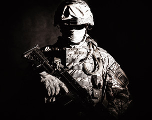 Half length portrait of special operations forces soldier, private military company guard in helmet, mask and uniform armed machine gun looking at camera. Contrast light, brown tone, black background