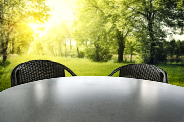 Wall Mural - empty round table and two black chairs with green trees ans sunshine summer garden background.