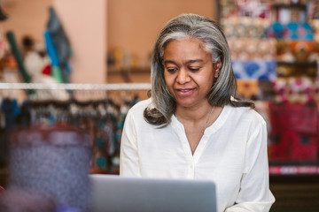 Wall Mural - Mature woman working on a laptop in her fabric shop 