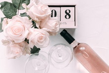 8 March. Happy Women's Day. Wooden Block Calendar. White Rose, Flowers. Bottle Of Pink Wine And Two Glasses Of Wine On A Soft Light Pink Wood Table, Flat Lay, Top View, Copy Space. Selective Focus 