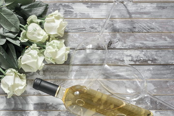 White roses and a bottle of white wine and two wine glasses on a wooden gray vintage table. Valentine's Day, 8 March, wedding, birthday. Flat lay, top view, copy space 