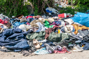 pile of old clothes and shoes dumped on the grass as junk and garbage, littering and polluting the e