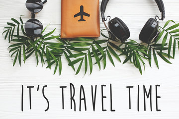 Wall Mural - It's Travel Time text on passport with plane, retro sunglasses and headphones on green palm leaves on white wood. modern travel and summer vacation flat lay