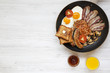 Full English breakfast in a pan with fried eggs, bacon, sausages, beans, toasts and orange juice on white wooden background with copy space, top view. Flat lay. From above.