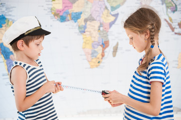 two beautiful caucasian kids in sailor striped shirts measure distance on world map with measuring tape