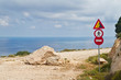 A road with a beautiful view on the Ionic sea, blocked by a fallen rock, several traffic signs warning and forbidding to use the road