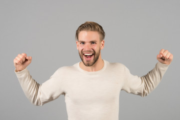 Wall Mural - Bearded man with winner gesture. Happy man with beard smile on unshaven face. Fashion model with blond hair in casual tshirt. Victory and success concept