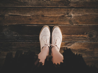 Selfie of feet in fashion beige leather flat brogues shoes on old wooden background, top view. Girl in pleated skirt. Trendy look. Hipster film filter