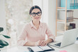© deagreez - Portrait of elegant classic charming pretty brunette cheerful woman in glasses sitting in modern office at desktop having computer organizer notebook on the table looking at camera