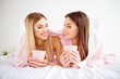 © deagreez - Portrait of pretty, charming, cute, cheerful, attractive, confident, successful girls in white and pink outfit having mugs with tea in hands, looking to each other, lying on stomach under plaid