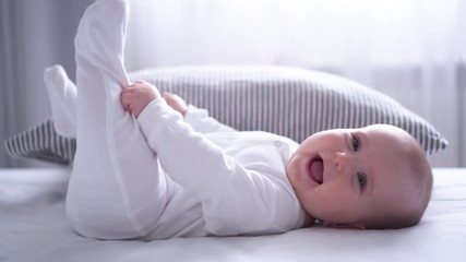 funny chubby baby playing with feet on bed