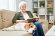 © Seventyfour - Portrait of elegant senior woman reading book sitting on couch and enjoying weekend with pet dog beside her in modern apartment interior, copy space