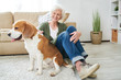 © Seventyfour - Full length portrait of happy  senior woman lovingly caressing pet dog sitting on floor in living room at home in modern apartment interior, copy space