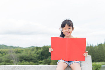 Beautiful smiling teenage girl in White blouse Sitting on a leak and read book, against green of summer park.