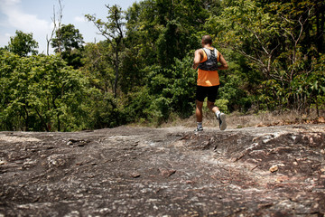 Trail running athlete moving through the wood in the rural road. Young fitness man running at tropical forest trail.