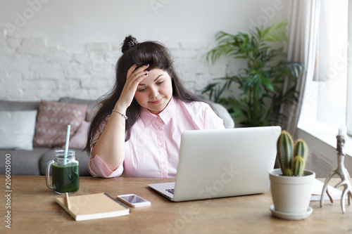 People, job, modern electronic gadgets and technologies. Frustrated young overweight brunette woman freelancer feeling tired and stressed while working remotely using laptop pc at home office - Buy this stock photo and