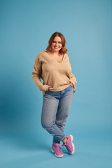 carefree curvy girl with hands in pocket posing at studio