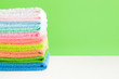 Stack of colorful, soft microfiber rags for different surfaces cleaning in kitchen, bathroom and other rooms. Towels for face and hands wiping. Empty place for text or logo on green background.